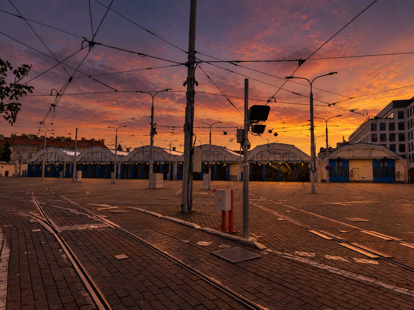 Oranžový západ slunce nad vozovnou a rozvětvenými tramvajovými kolejemi