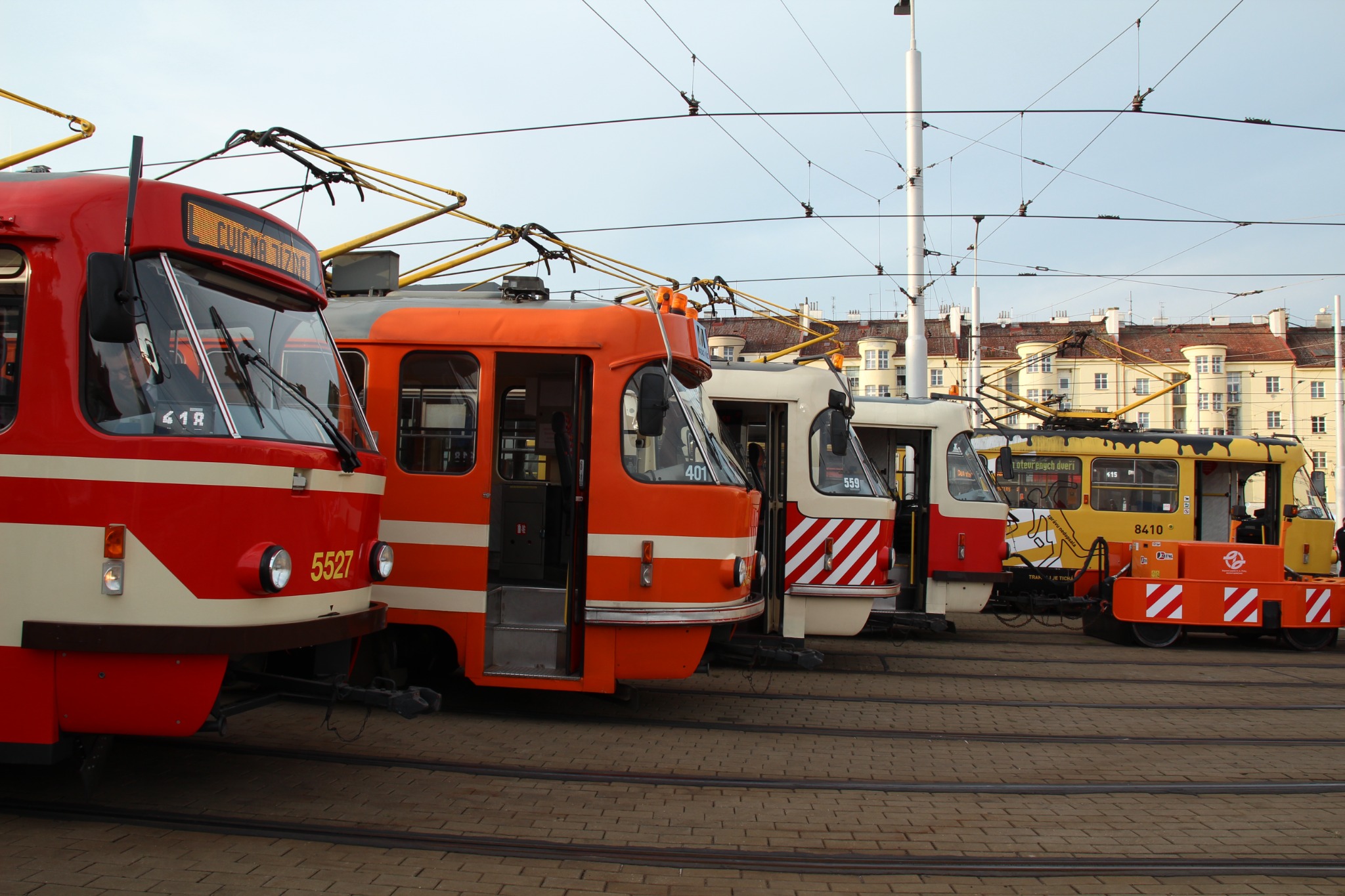Řada tramvají různých barev odstavených pod trolejovým vedením ve vozovně
